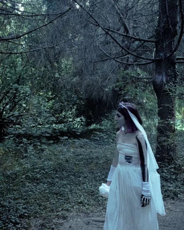 Darlie Ole in abito bianco in un bosco in penombra