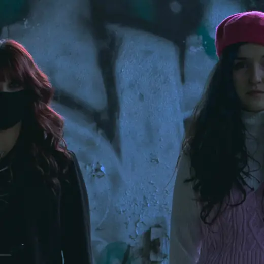 Due ragazze con berretto rosa davanti a un muro graffitato, luce notturna