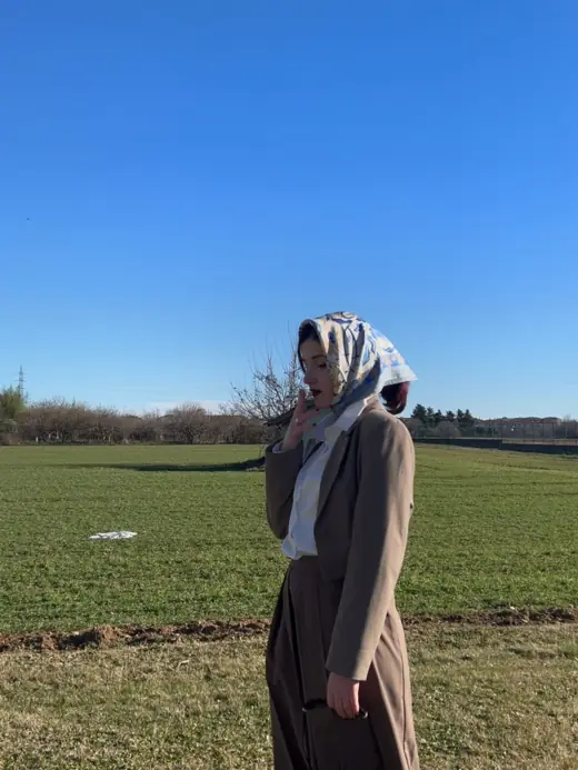 Darlie Ole con foulard in testa e cappotto in un campo
