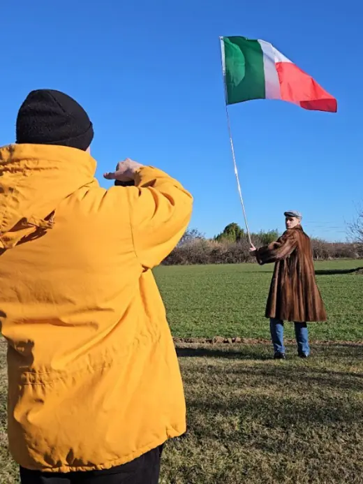 Ragazzo in giacca gialla saluta il tricolore in un campo