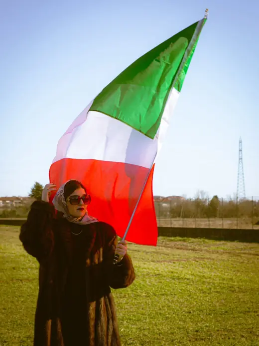 Darlie Ole in pelliccia regge il tricolore sotto il cielo azzurro